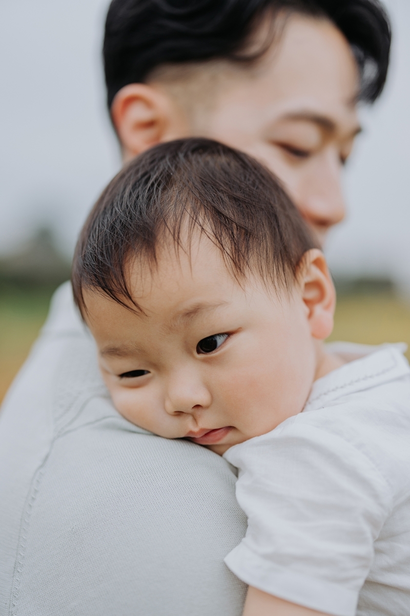 little boy resting on his father's shoulder during family photoshoot in a field in summer-Stockport Family photography