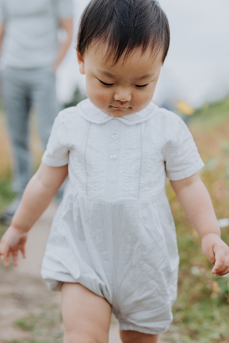 little boy looking down as he walks away from his dad in a sunflower field-family photograher stockport