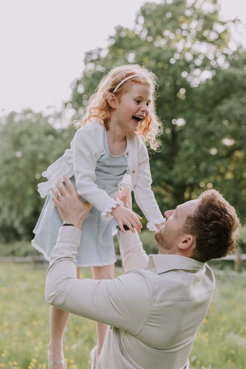 Auburn haired girl being lifted and thrown into the air by her father on a sunny day-Stockport Family photographer